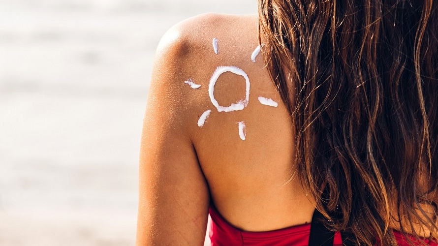 Frau mit Sonnencreme auf Schulter Rücken einer Frau im Bikini mit Zeichnung einer Sonne aus Sonnencreme auf der Schulter